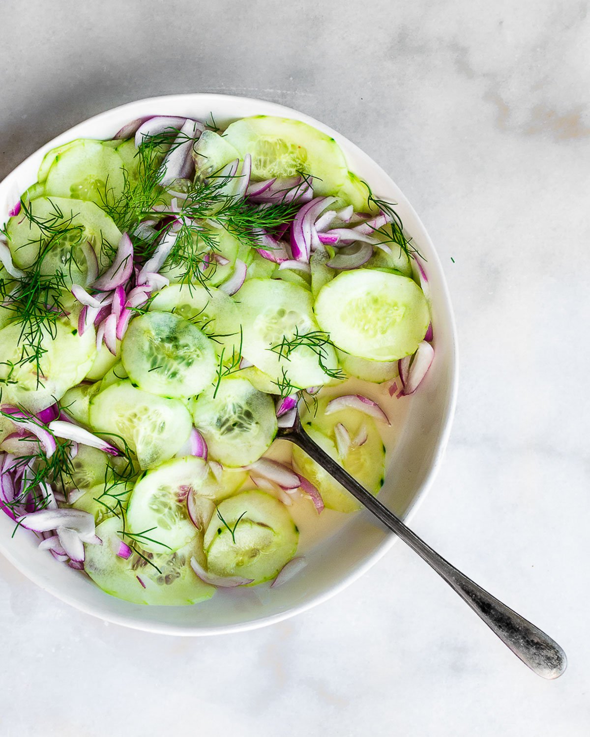 Cucumber Dill Salad in a white bowl on a marble background