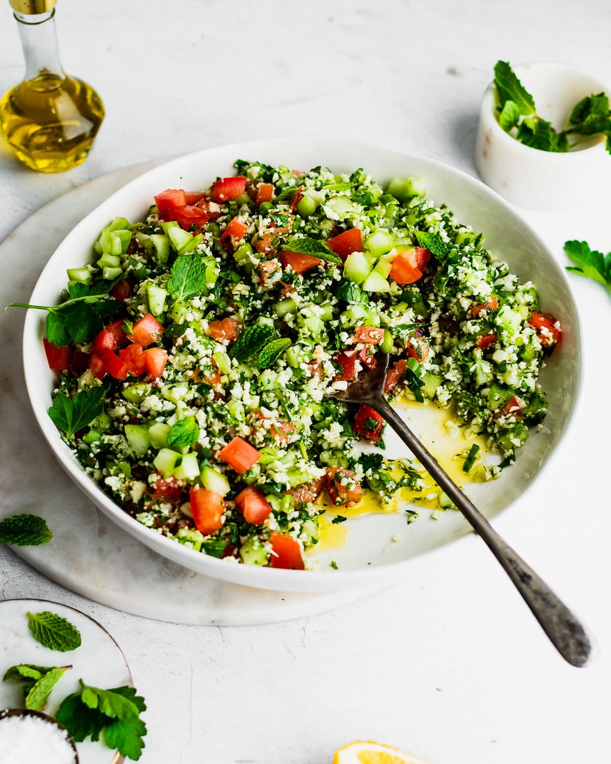 Cauliflower tabbouleh in a white bowl, garnished with mint, lemon and parsley