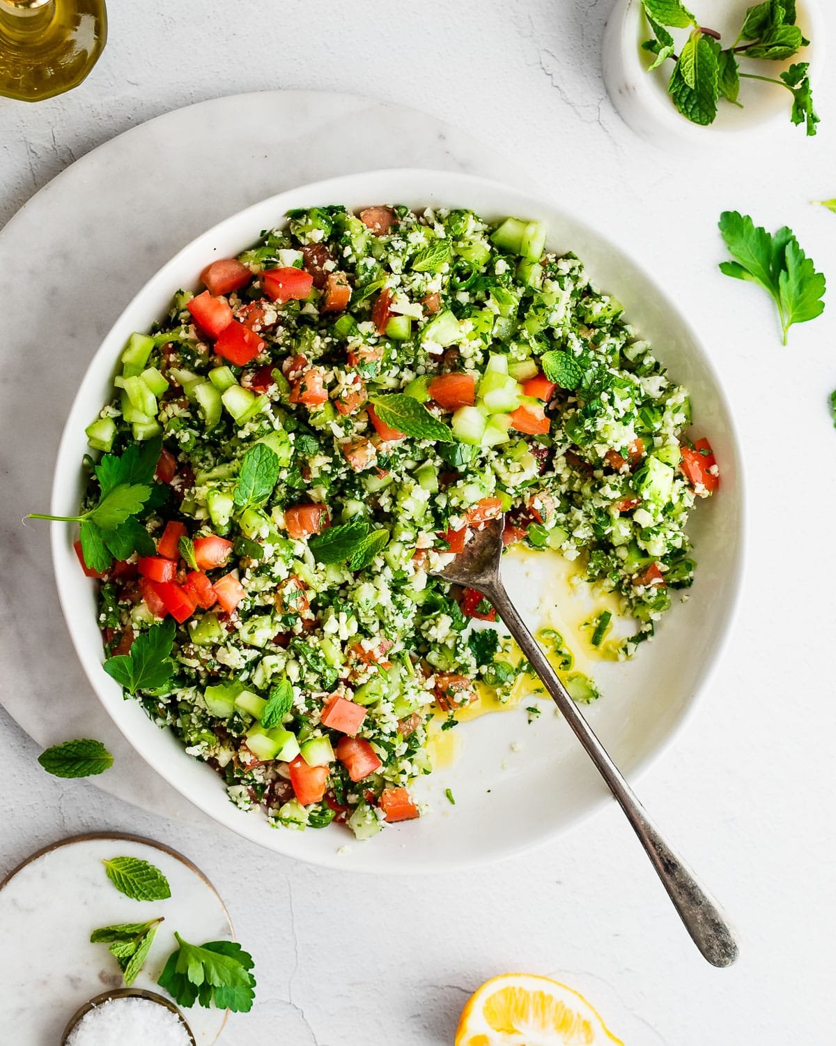 Cauliflower tabbouleh in a white bowl, garnished with mint, lemon and parsley