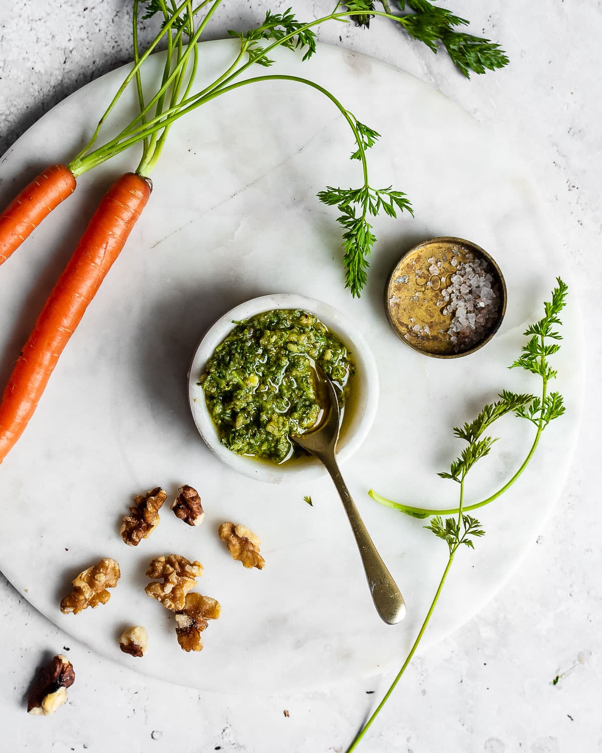 Carrot top pesto in a white marble bowl on white surface with carrots
