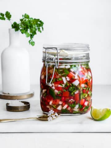 fermented salsa in a glass jar, garnished with cilantro flowers and lime