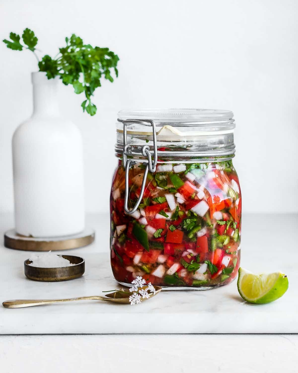 fermented salsa in a glass jar, garnished with cilantro flowers and lime