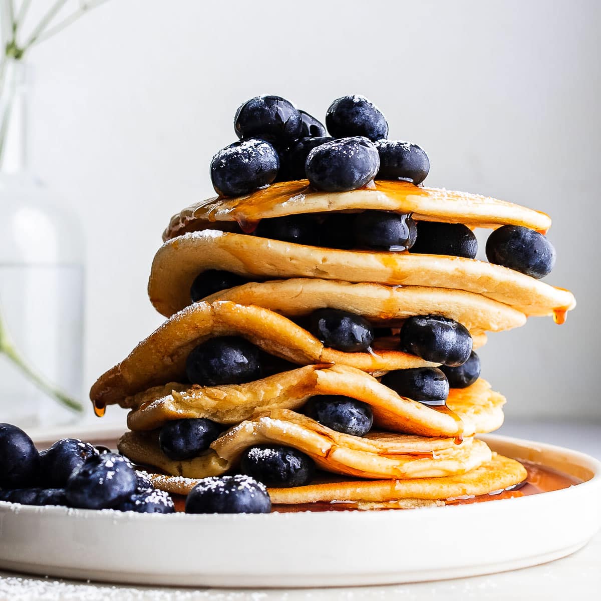 Stack of einkorn pancakes garnished with blueberries and drizzled with maple syrup on white plate.