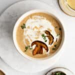 Wild mushroom soup drizzled with cream and sprinkled with fresh thyme in a white bowl