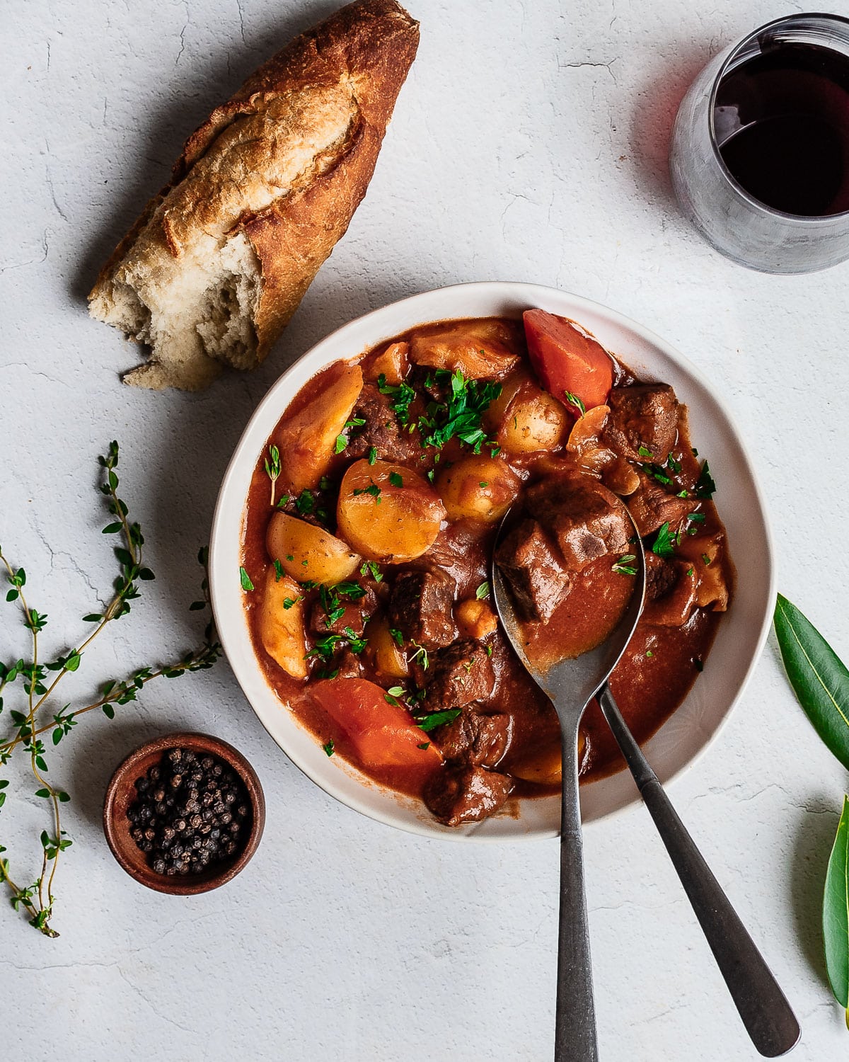 Bison stew in a white bowl, garnished with bay leaf, thyme and a baguette