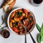 Bison stew in a white bowl, garnished with bay leaf, thyme and a baguette