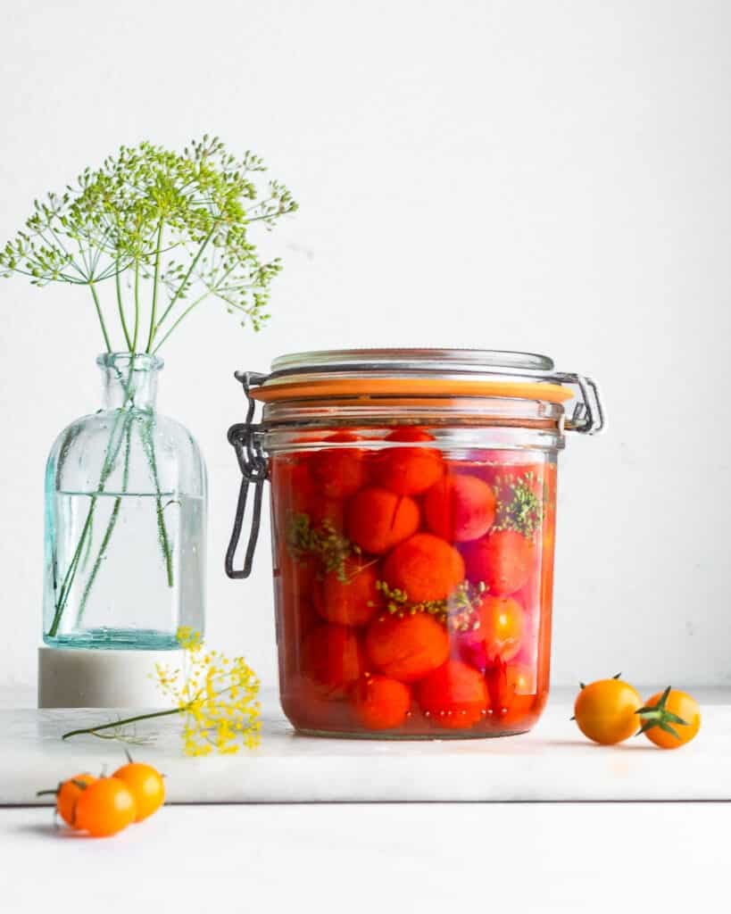 Fermented cherry tomatoes in a clip-top jar, with dill flowers in the background