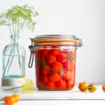 Fermented cherry tomatoes in a clip-top jar, with dill flowers in the background