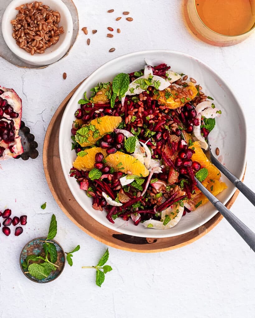 Emmer and beet salad garnished with fennel, oranges and mint in a white bowl