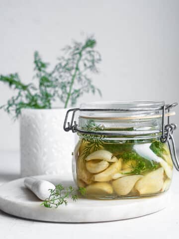 Fermented garlic and dill in a glass jar on a white surface
