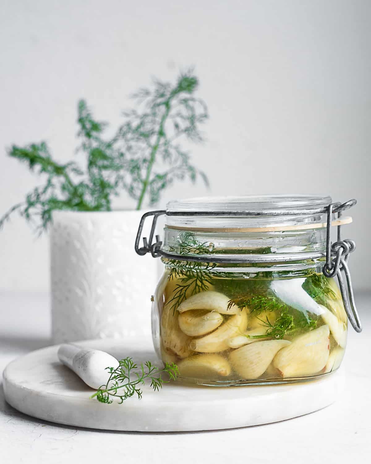 Fermented garlic and dill in a glass jar on a white surface