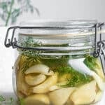 Fermented garlic and dill in a glass jar on a white surface