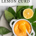 Lemon curd in a white bowl setting on citrus leaves