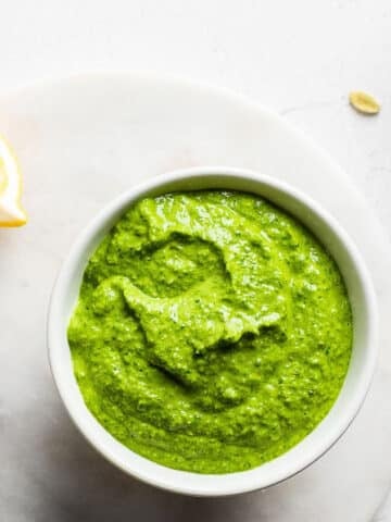 Mustard green pesto in a white bowl on a marble surface