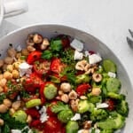 savory yogurt bowl garnished with feta, herbs and hazelnuts in a white bowl on a white surface