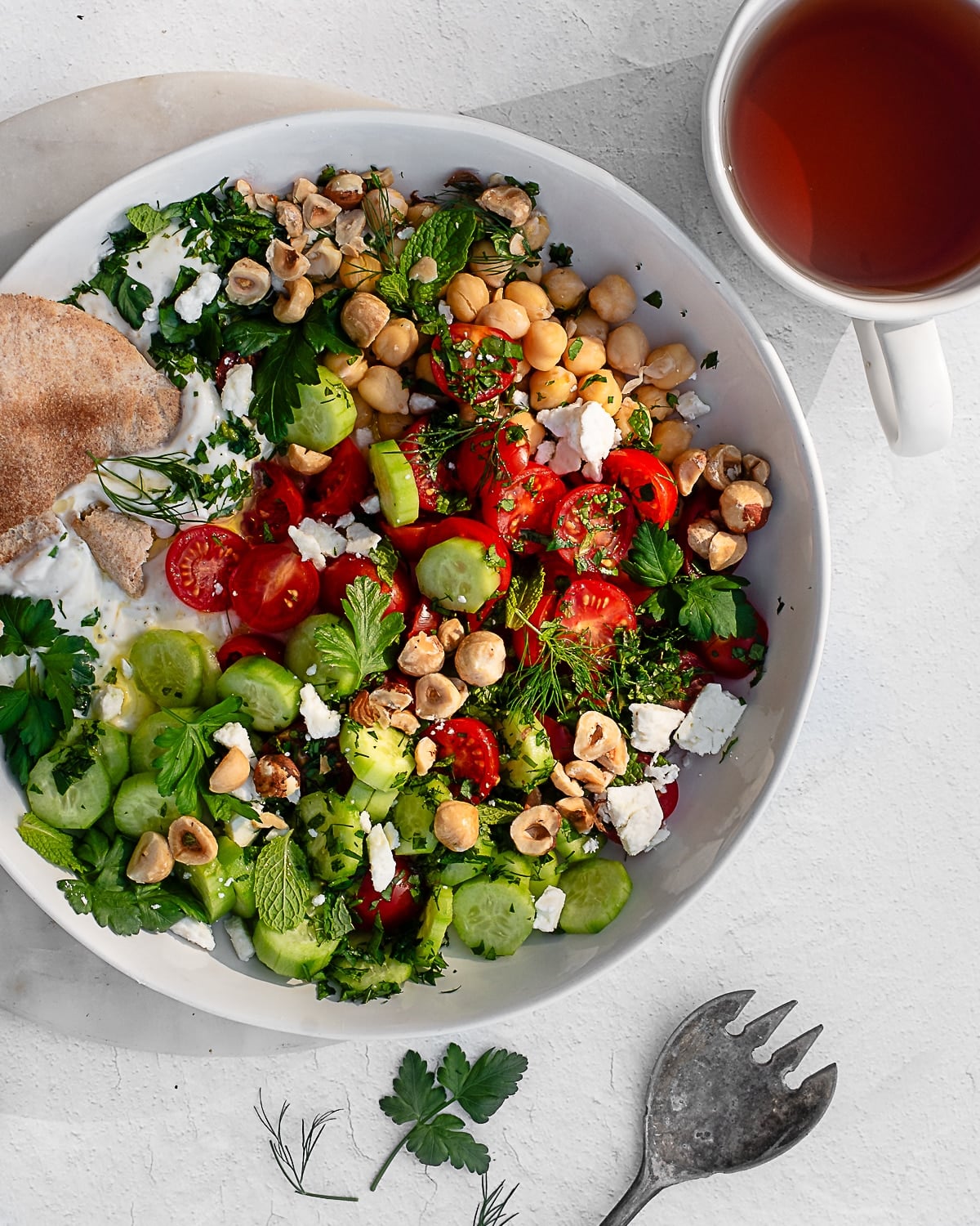 savory yogurt bowl garnished with feta, herbs and hazelnuts in a white bowl on a white surface