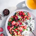 A pink bowl filled with yogurt, strawberries, mint, lemon balm, walnuts and cacao nibs