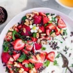 A pink bowl filled with yogurt, strawberries, mint, lemon balm, walnuts and cacao nibs